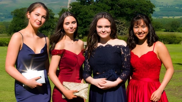 Vier junge Frauen in formeller Kleidung stehen vor einer bergigen Landschaft auf dem Gelände von St. Brigid's College.