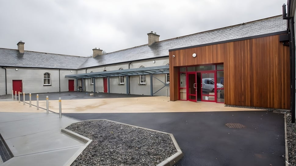 Das Hauptgebäude von St. Brigid's College mit roter Tür steht auf einem gepflasterten Hof mit Kiesakzenten.