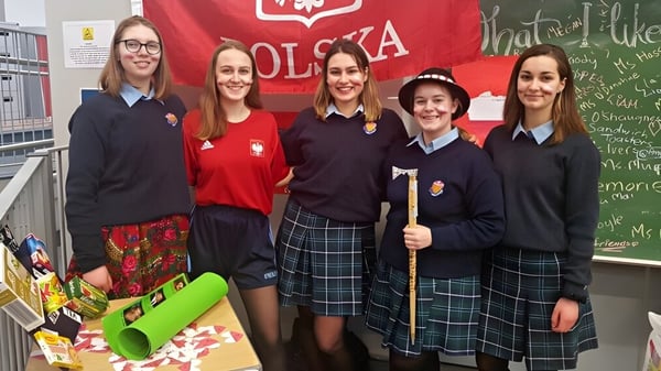 Eine Gruppe von Schülerinnen des St. Brigid's College steht vor einer roten und weißen Flagge mit polnischem Adleremblem.