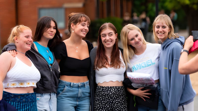 Eine Gruppe junger Schülerinnen steht lachend zusammen auf dem Außengelände der St. Catherine's School vor Backsteingebäuden und Grünflächen.