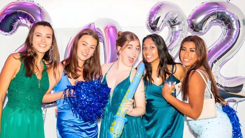 Fünf Schülerinnen in bunten Kleidern posieren vor großen lila und silbernen 21-Ballons auf dem Gelände der St. Catherine's School.