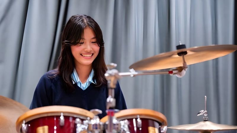 Eine Schülerin der St. Catherine's School spielt begeistert Schlagzeug auf einer Bühne mit grauem Vorhang im Hintergrund.