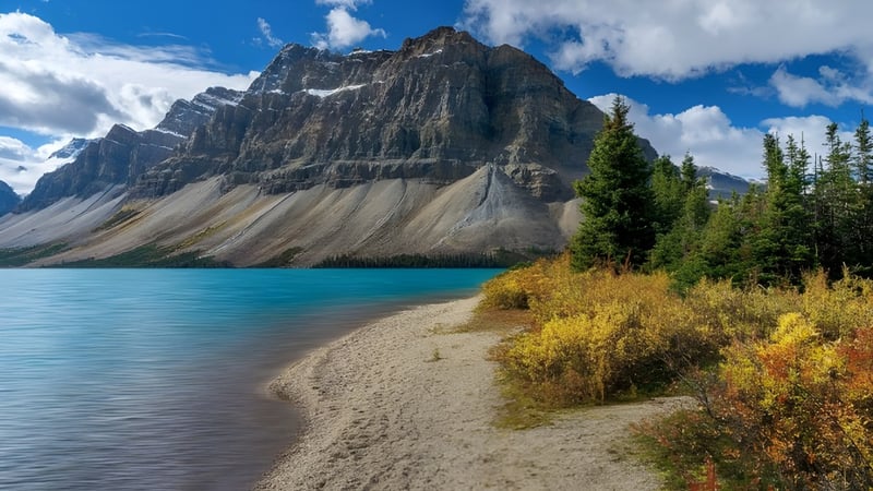 Ein ruhiger türkisfarbener Bergsee mit herbstlich farbigen Bäumen und Berggipfeln auf dem Gelände des St. Charles College.