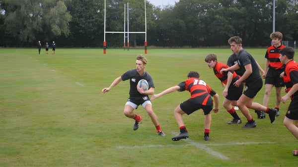 Rugbyspieler der St. Christopher School in roten und schwarzen Trikots spielen auf einem Spielfeld mit Torpfosten.