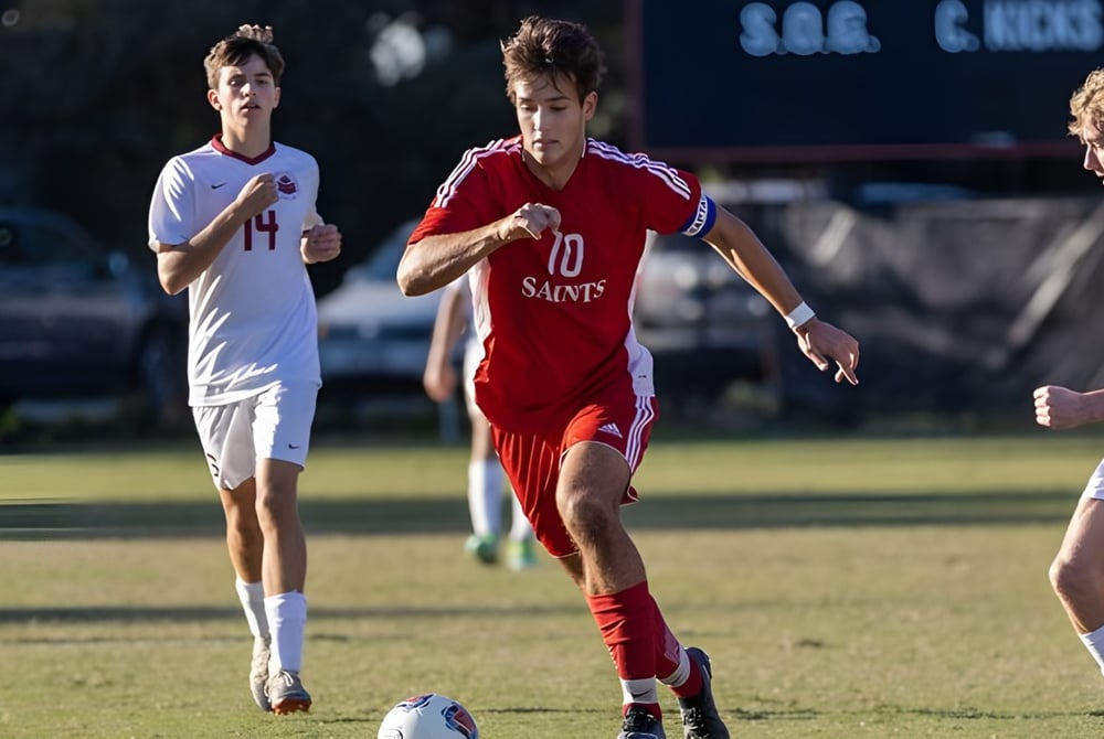 Drei Fußballspieler in Aktion auf dem Spielfeld der St. Christopher’s School mit einer Anzeigetafel im Hintergrund.