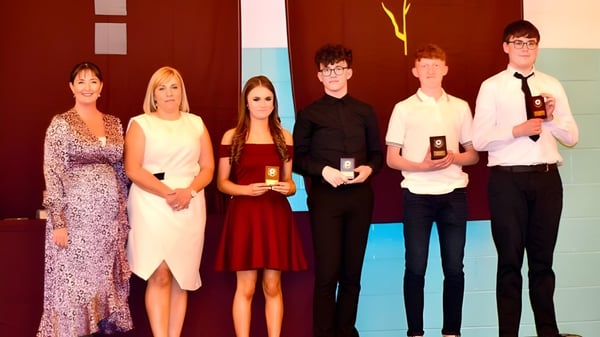 Eine Gruppe von sechs Personen steht bei einer Veranstaltung vor einem bunten Hintergrund auf dem Campus der St. Ciarán’s Community School.
