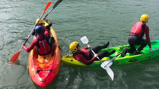 Schüler der St. Ciarán’s Community School paddeln in bunten Kajaks auf einem See inmitten einer naturnahen Landschaft.
