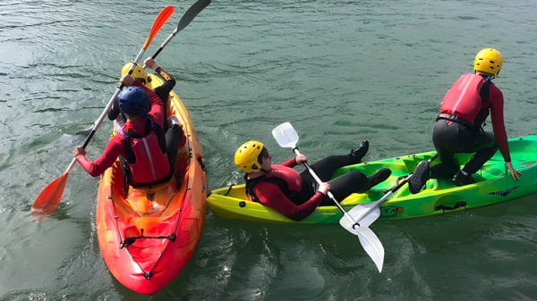 Schüler der St. Ciarán’s Community School paddeln in bunten Kajaks auf einem See in natürlicher Umgebung.
