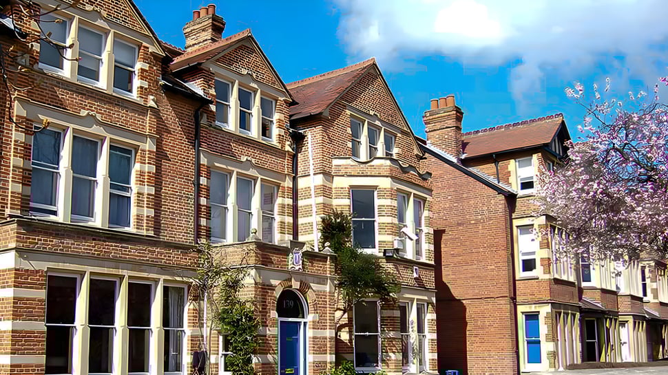Das Backsteingebäude der St. Clare’s School ist von blühenden Bäumen und einem klaren Himmel umgeben.