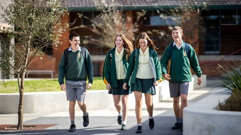 Vier Schüler der St. Clare’s School gehen zusammen auf dem Schulgelände mit einem Gebäudekomplex im Hintergrund.