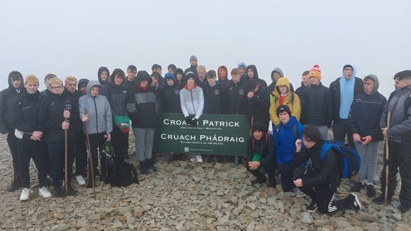 Eine Gruppe Schülerinnen und Schüler vom St. Coleman's College steht vor dem Schild Croagh Patrick in einer felsigen Berglandschaft.