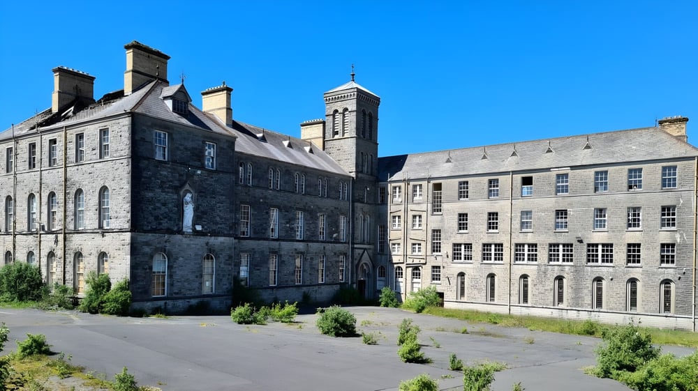 Das historische Gebäude mit mehreren Türmen und Schornsteinen auf dem Campus von St. Coleman's College ist von grüner Landschaft umgeben.