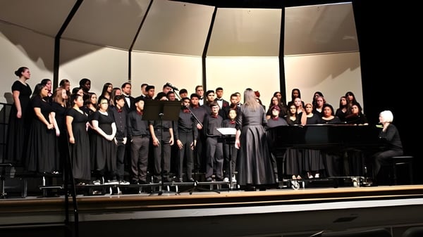 Schüler des St. Colmans College stehen in formeller Kleidung zusammen auf einer Bühne und singen gemeinsam mit einem Klavier im Vordergrund.