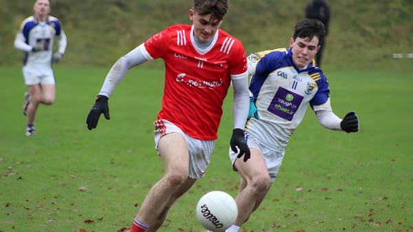 Zwei Fußballspieler in roten und blauen Trikots spielen auf dem Sportplatz von St. Colmans College.