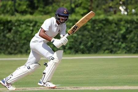 Ein Cricket-Spieler in weißer Uniform hält einen Schläger auf dem Spielfeld des St. Columba's College.