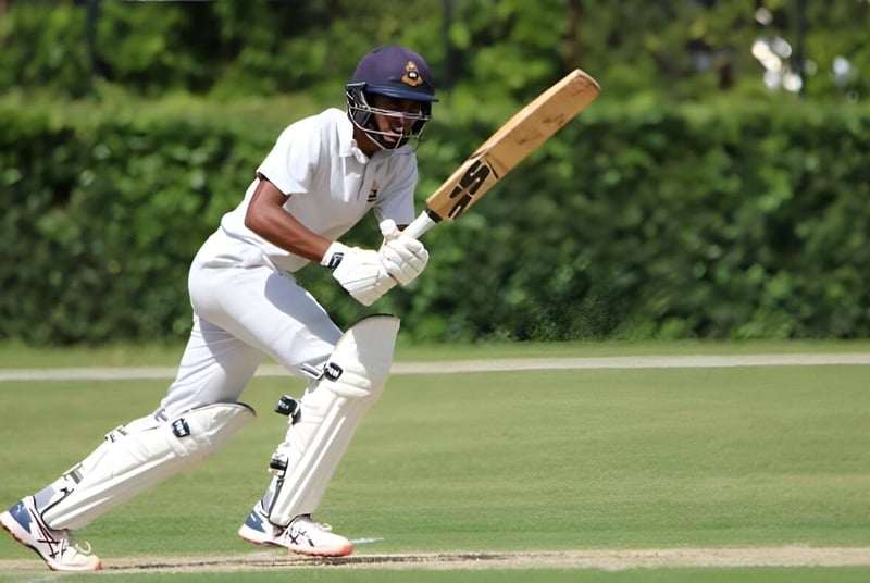 Ein Cricket-Spieler in weißer Uniform hält einen Schläger auf dem Spielfeld des St. Columba's College.