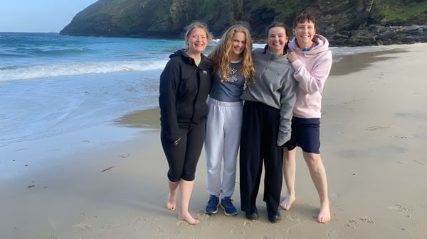 Vier Schülerinnen des St. Columba's College stehen gemeinsam am Strand mit Blick auf das Meer und felsige Klippen.