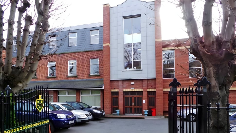 Das Gebäude von St. Conleths College zeigt einen mehrstöckigen Backsteinbau mit einem modernen Glasanbau und kahlen Bäumen im Hintergrund.