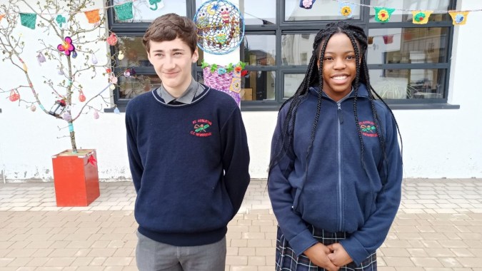 Zwei Schülerinnen und Schüler in Schuluniform stehen vor einem bunt dekorierten Gebäude auf dem Campus des St. Conleths College.