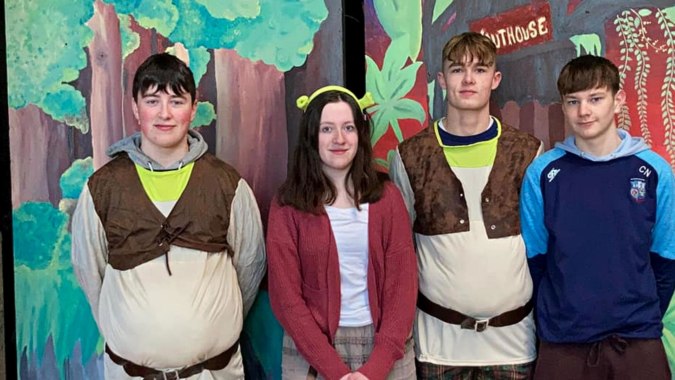 Vier Schülerinnen und Schüler stehen vor einer bunten Graffiti-Wand auf dem Gelände des St. Cuan’s College.