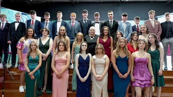 Eine große Gruppe formal gekleideter Schülerinnen und Schüler auf einer Zeremonie am St. Cuan’s College steht vor einer Bühne.