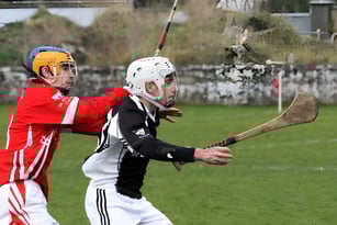 Zwei Spieler in Sportkleidung spielen auf dem Sportplatz von St. Cuan’s College vor einem Hintergrund mit Gebäude.