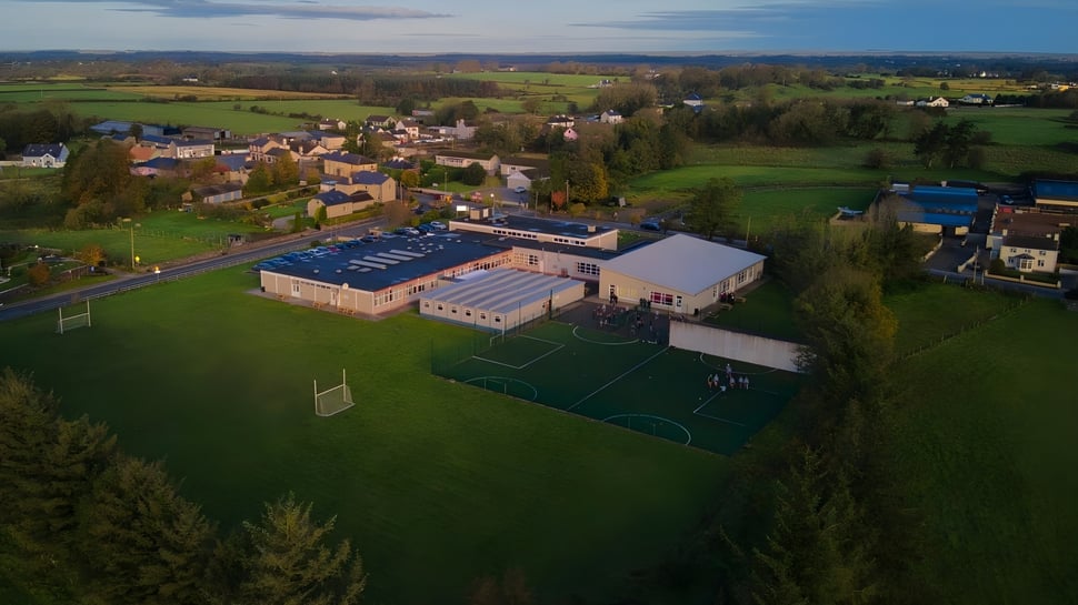 Das Sportgelände von St. Cuan’s College liegt am Rand eines grünen Dorfes mit Hügeln und Wäldern im Hintergrund.