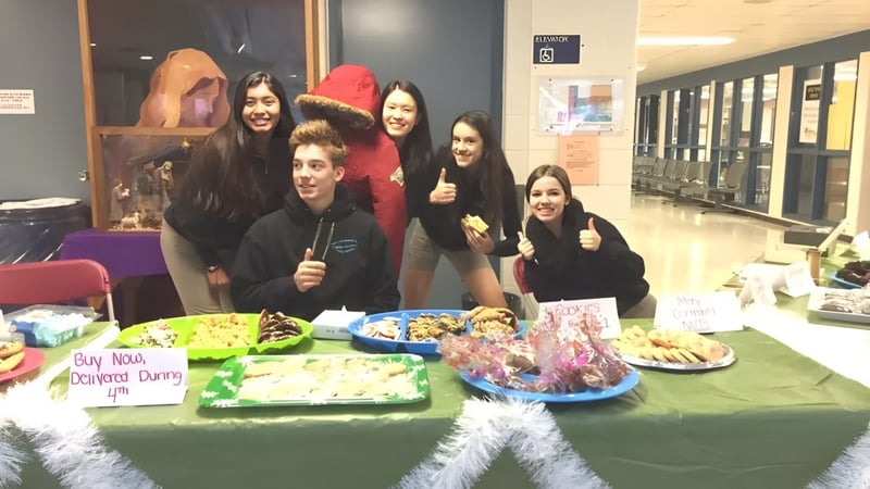 Schüler der St. David Catholic Secondary School verkaufen Muffins an einem Tisch mit dem Schild 'Buy Muffins Donate Diapers'.