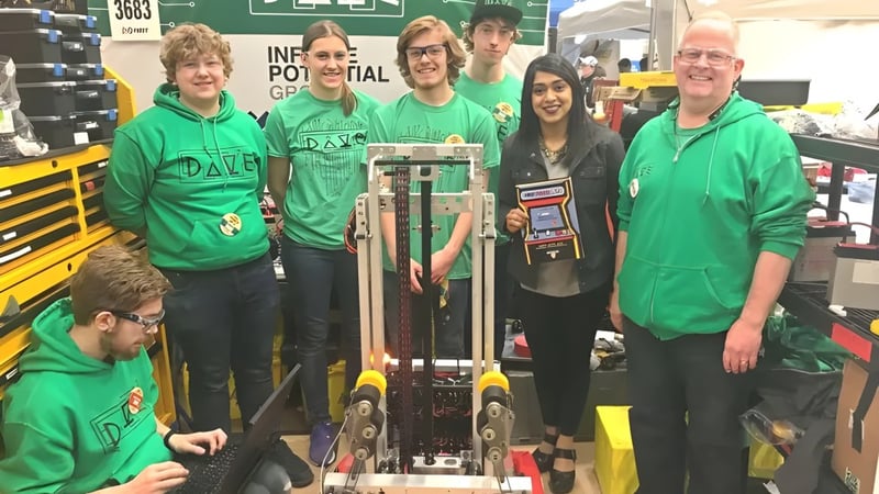 Eine Gruppe Schülerinnen und Schüler der St. David Catholic Secondary School steht vor einem großen grünen Banner mit der Aufschrift FIRST ROBOTICS COMPETITION.