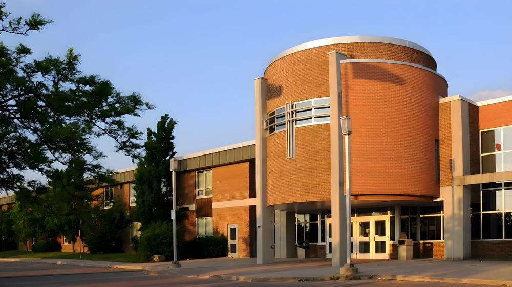 Das moderne Backsteingebäude mit einem runden Turm der St. David Catholic Secondary School steht umgeben von Grünflächen unter blauem Himmel.