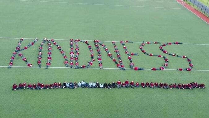 Eine große Gruppe von Schülerinnen und Schülern formt das Wort KINDNESS auf dem Sportplatz von St. David's C.B.S.