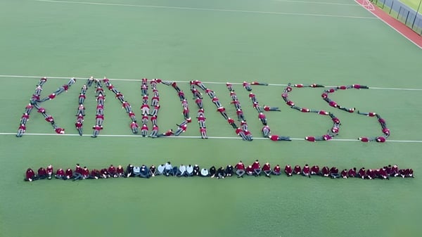 Eine große Gruppe von Schülerinnen und Schülern der St. David's C.B.S. formt auf dem grünen Sportfeld das Wort Kindness.