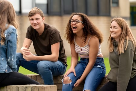Eine Gruppe von Schülerinnen und Schülern unterhält sich lebhaft vor dem Gebäude und Grünflächen des St. David’s College.