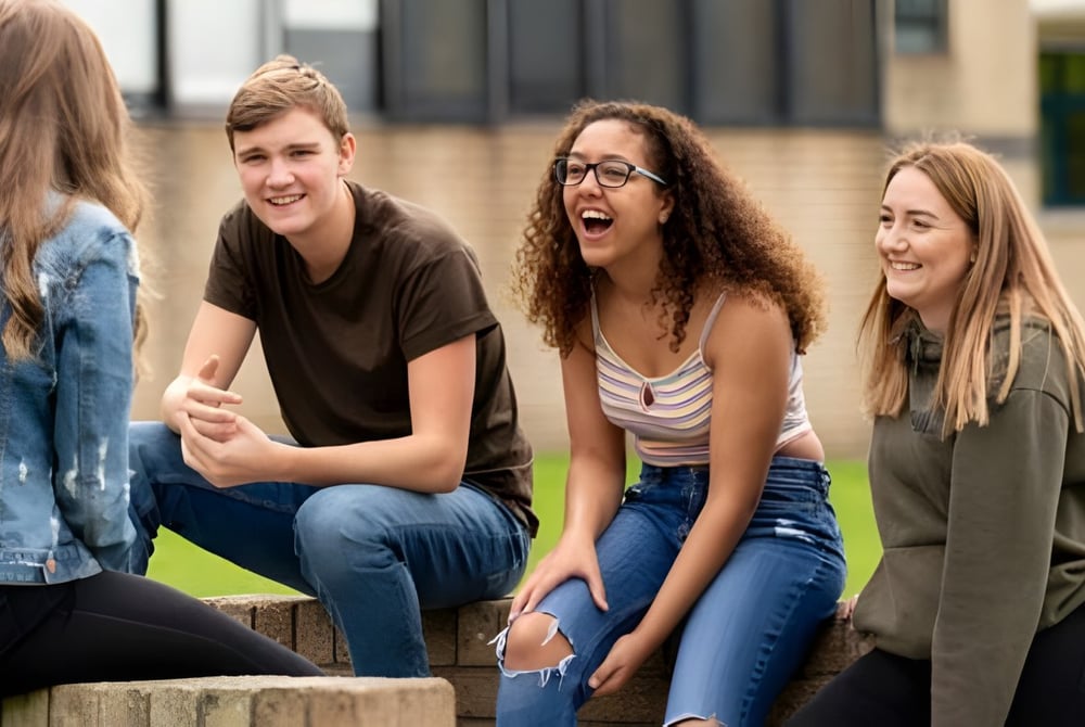 Eine Gruppe von Schülerinnen und Schülern unterhält sich lebhaft vor dem Gebäude und Grünflächen des St. David’s College.