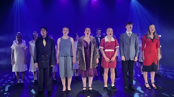 Eine Gruppe von Schülerinnen und Schülern der St. Dominic's Grammar School präsentiert eine Modenschau auf einer Bühne mit blau-violetter Beleuchtung.