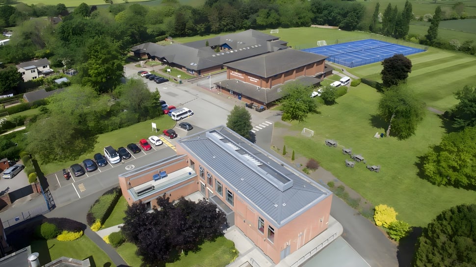 Das mehrstöckige Backsteingebäude der St. Dominic's Grammar School mit blauer Solardachanlage steht auf einer Wiese umgeben von Bäumen.