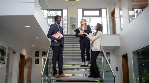 Drei Personen stehen auf einer Treppe in einem modernen Gebäude auf dem Campus der St. Dominic's Grammar School.