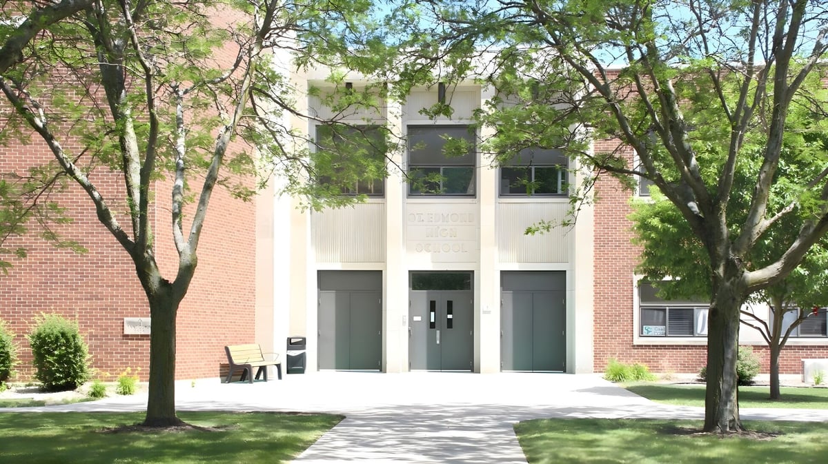 Das moderne Backsteingebäude mit großen Fenstern von St. Edmond Catholic School ist von grüner Vegetation und Bäumen umgeben.