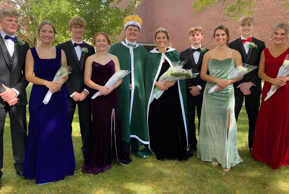 Eine Gruppe formell gekleideter Schülerinnen und Schüler steht im Grünen vor einem Ziegelgebäude auf dem Gelände der St. Edmond Catholic School.