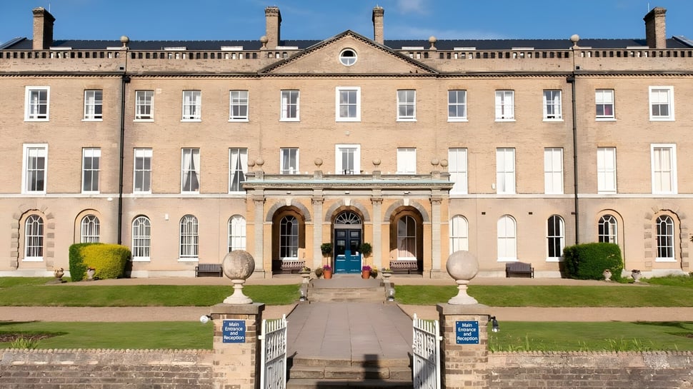 Das Gebäude von St. Edmund’s College mit einem zentralen Eingang und symmetrischen Flügeln ist von einem gepflegten Garten mit Steinwegen umgeben.