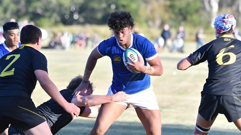 Eine Gruppe von Schülern spielt Rugby auf dem Sportfeld des St. Edmund’s College mit Bäumen und Gebäuden im Hintergrund.