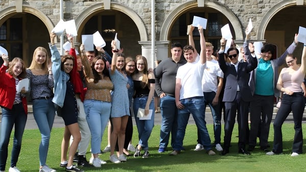 Eine Gruppe Schülerinnen und Schüler steht vor einem historischen Stein-Gebäude auf dem Campus der St. Edmunds School und hebt die Hände.