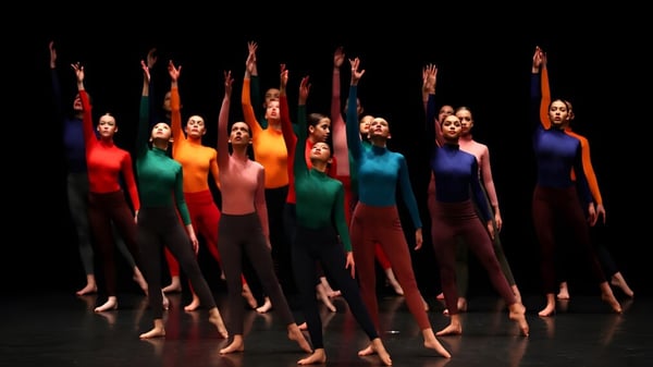 Eine Gruppe Tänzerinnen der St. Edmunds School führt auf einer dunklen Bühne eine synchronisierte Choreographie mit erhobenen Armen auf.