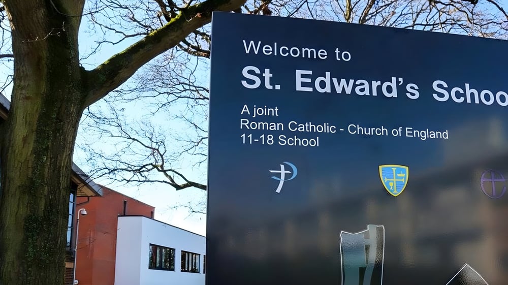 Willkommensschild der St. Edward's School in Poole mit Kreuz- und Schild-Logo vor dem Backsteingebäude.