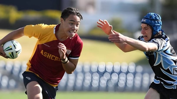 Zwei Rugbyspieler in einem Spiel auf dem Sportfeld der St. Felix School, wobei ein Spieler im roten Trikot versucht, den Tackling des Gegners zu entkommen.