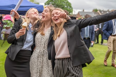 Schülerinnen der St. Felix School machen ein Selfie im Freien vor einer Wiese mit Zelten.