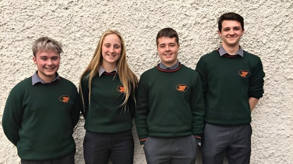 Vier Schülerinnen und Schüler stehen vor einer weißen Wand mit grünen Pullovern auf dem Campus von St. Fergal’s College.