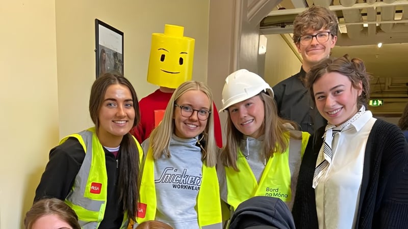 Eine Gruppe Schülerinnen und Schüler des St. Finian’s College in Sicherheitswesten und Helmen posiert vor einer gelben Cartoonfigur.