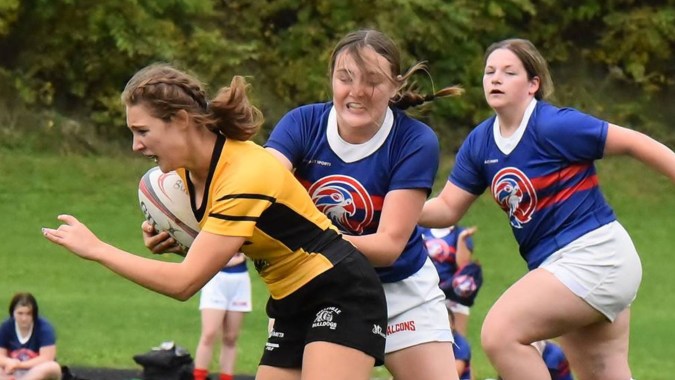 Drei Schülerinnen in Sportkleidung nehmen an einer Outdoor-Aktivität auf dem Sportplatz des St. Finian’s College, Mullingar, teil.