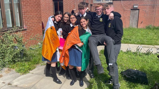 Eine Gruppe Schülerinnen und Schüler in Schuluniformen steht vor einem Backsteingebäude auf dem Gelände von St. Finian’s Community College.